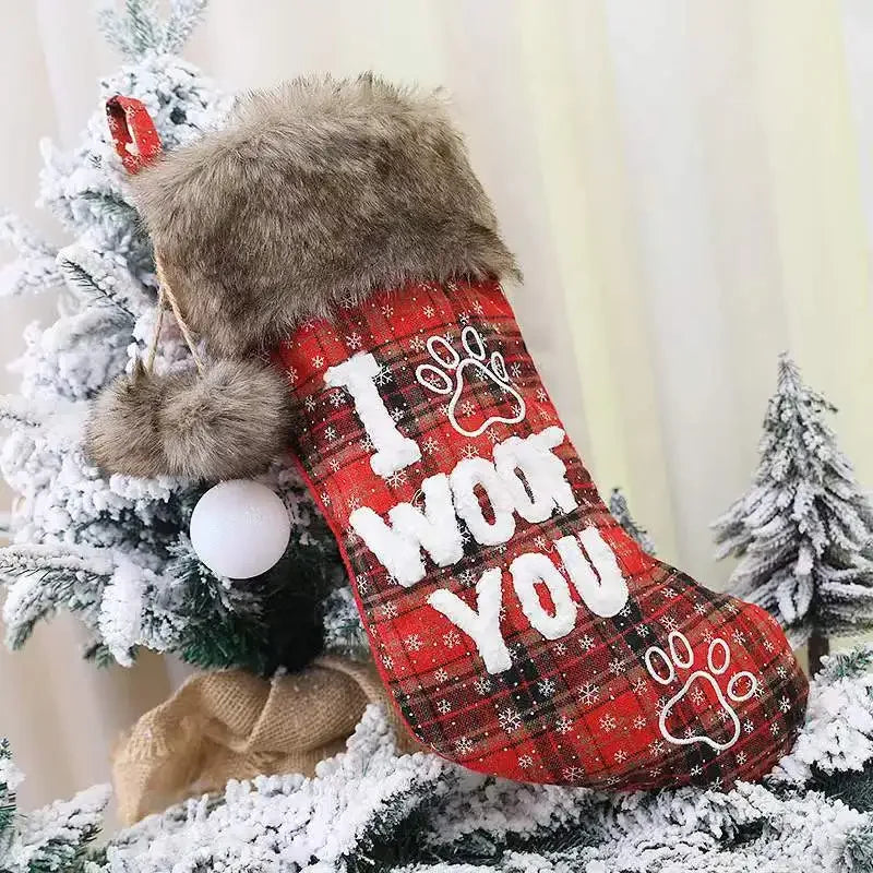 Red plaid Christmas stocking with 'I Woof You' text and paw print, hanging on a tree.
