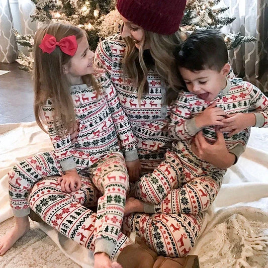 Three children in matching festive pajamas sitting together in front of a Christmas tree.
