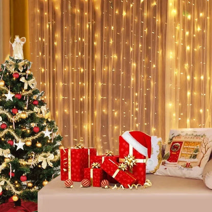 Decorated Christmas tree with presents and a Santa hat in front of a curtain with string lights.