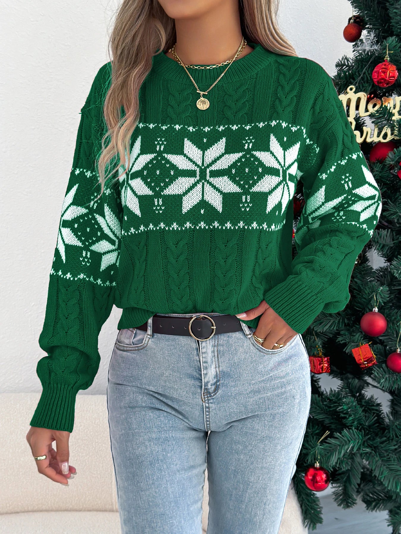 Person wearing a green sweater with snowflake pattern in front of a decorated Christmas tree.