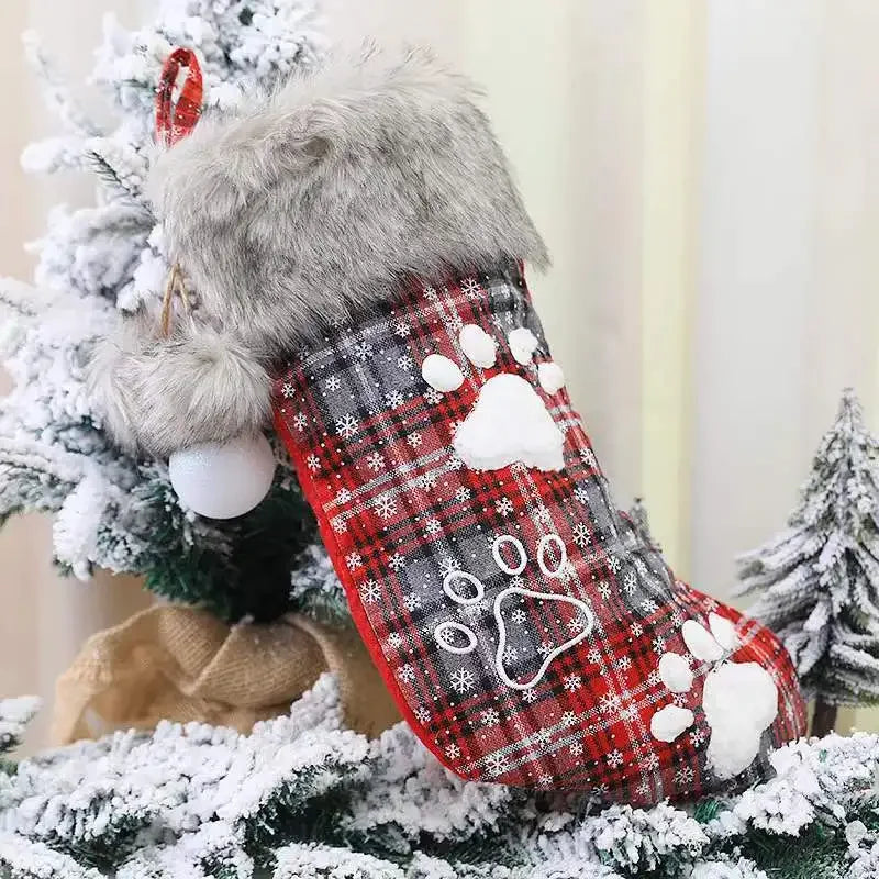 Red plaid Christmas stocking with paw prints on a snowy tree background