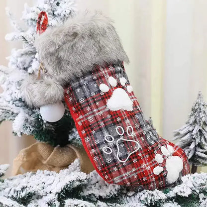 Red plaid Christmas stocking with paw prints on a snowy tree background