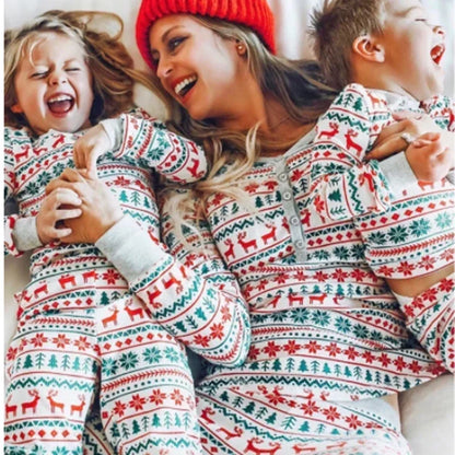 Woman and two children wearing matching Christmas pajamas with reindeer and tree patterns.