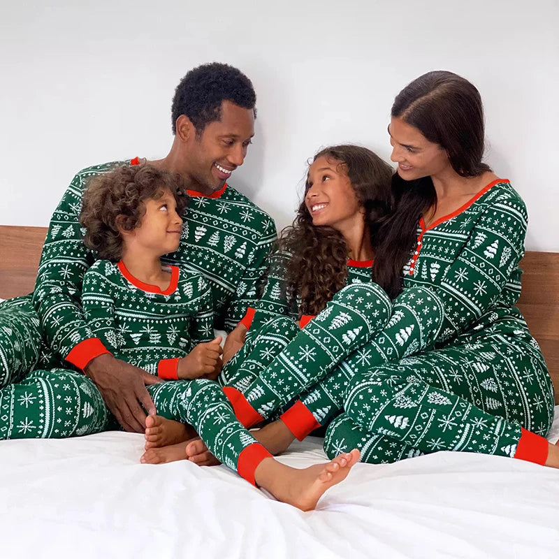 Family of four wearing matching green and red Christmas pajamas sitting on a bed.